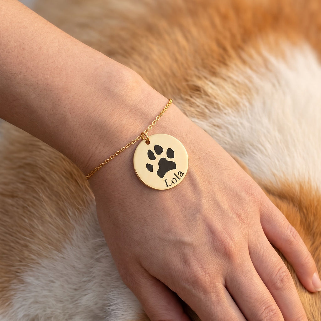 Pulsera dorada con la huella de un perro y el nombre Lola, en la muñeca