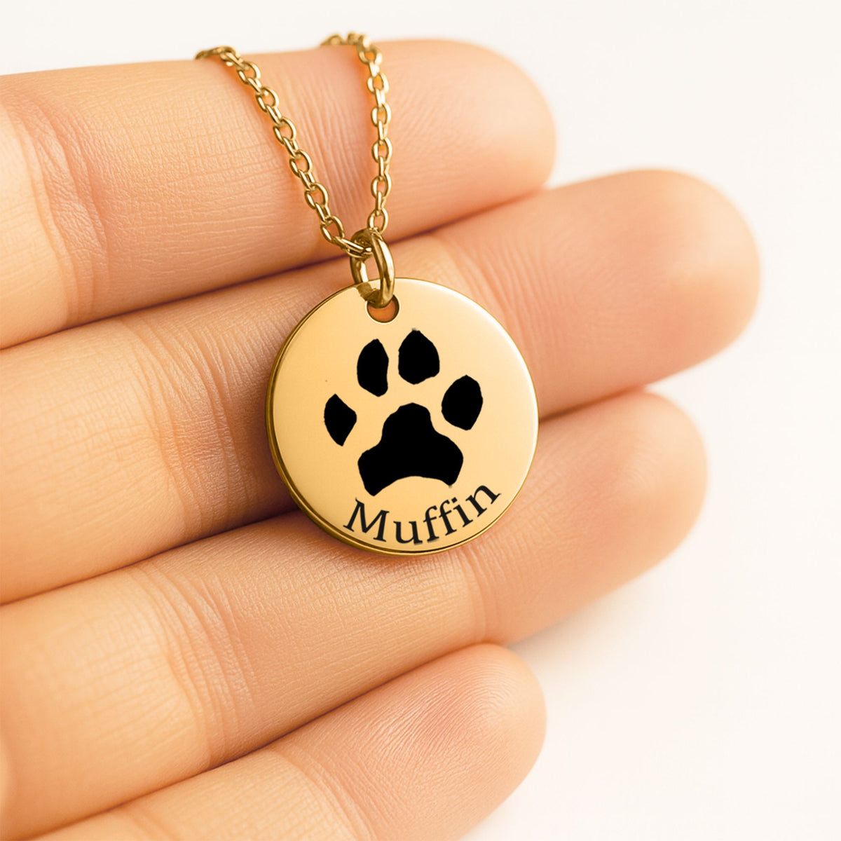 Collar dorado con la huella de un perro grabada y el nombre Muffin, sobre la mano
