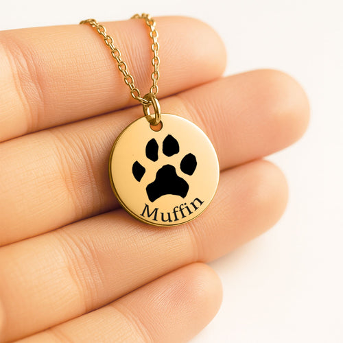 Collar dorado con la huella de un perro grabada y el nombre Muffin, sobre la mano